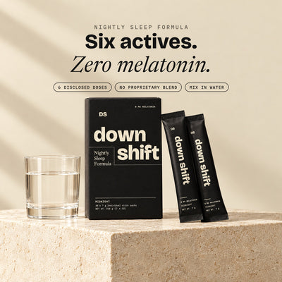 Downshift Nightly Sleep Formula carton and two stick packs beside a glass of water. Six actives, zero melatonin.